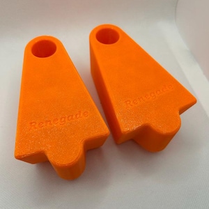 May include: Two bright orange, wedge-shaped plastic blocks with a circular hole at the top. Each block features the word Renegade embossed on the front surface. The objects have a smooth, matte finish and a distinct, angular, tapered design.