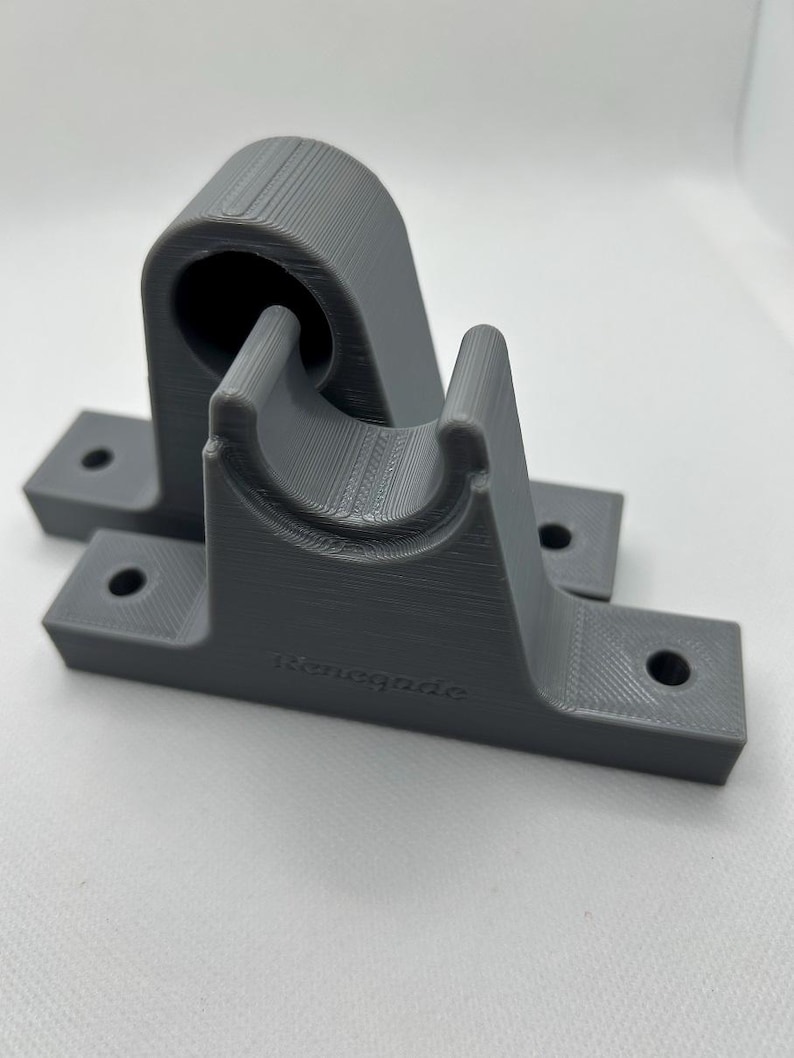 Puede incluir: Dos soportes grises impresos en 3D. Cada soporte tiene una base con dos agujeros para el montaje y una secci&oacute;n curva dise&ntilde;ada para sujetar un objeto cil&iacute;ndrico. El texto "renegade" est&aacute; impreso en la base de un soporte.