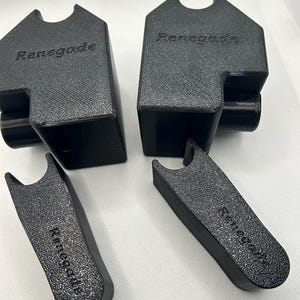 May include: Four black, textured, 3D-printed objects. Two are rectangular with a curved top and the word "Renegade" printed on them. The other two are larger, with a similar texture and the word "Renegade" printed on them.