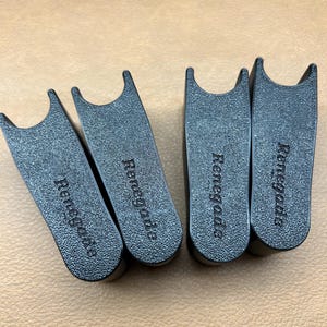 May include: Four black, textured plastic objects with a curved top and the word "Renegade" printed on them. The objects are arranged on a light brown surface.