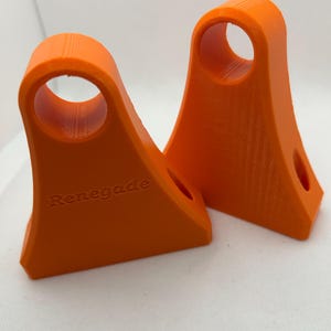 May include: Two bright orange, 3D-printed objects. Each has a curved top with a circular hole and a flat base. The word "Renegade" is printed on one. The objects are likely components or supports.