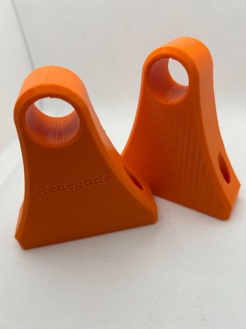 May include: Two bright orange, 3D-printed objects. Each has a curved top with a circular hole and a flat base. The word "Renegade" is printed on one. The objects are likely components or supports.