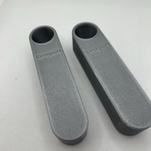 May include: Two gray, rectangular bottle stoppers with a textured surface and a circular opening at the top. The word "Renegade" is printed on the side of each stopper.