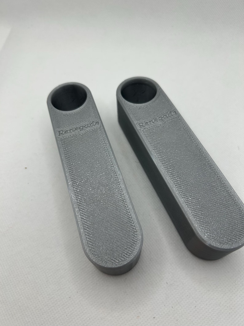 May include: Two gray, rectangular bottle stoppers with a textured surface and a circular opening at the top. The word "Renegade" is printed on the side of each stopper.