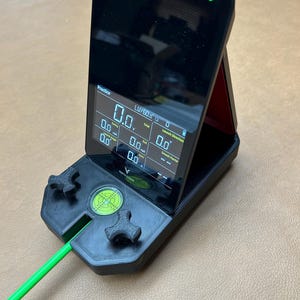 以下が含まれることがあります： 数値データを表示する画面を備えた黒い電子デバイス。スポーツや測定用かもしれません。デバイスには緑色の電源インジケーターと緑色のケーブルがあります。ベースには水準器と2つの装飾的な形があります。