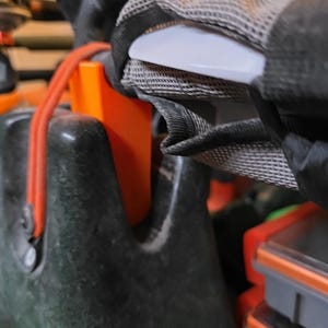 May include: Close-up of a black and orange kayak or boat component. The image shows a white handle, a mesh strap, and an orange plastic piece. A red rope is also visible. The components appear to be part of a larger system.