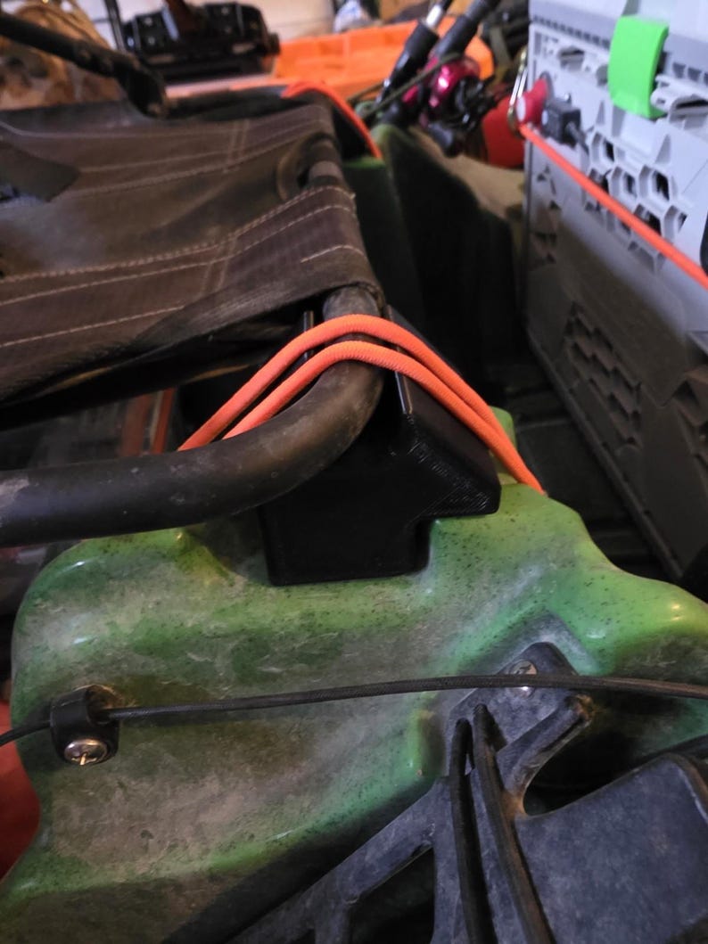 May include: Close-up of a kayak seat with orange rope and black hardware. The seat is black and attached to a green kayak. The image shows the details of the seat's construction and the kayak's components.