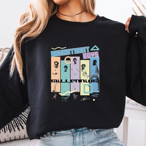 May include: Black long-sleeve sweatshirt featuring a colorful graphic of the Backstreet Boys. The graphic includes the text "BACKSTREET BOYS" and "MILLENNIUM" with images of the band members and their signatures.