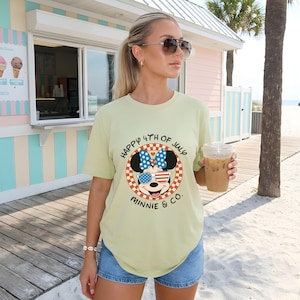 Light green Minnie Mouse 4th of July tee with stars and stripes, worn by a woman on a boardwalk.