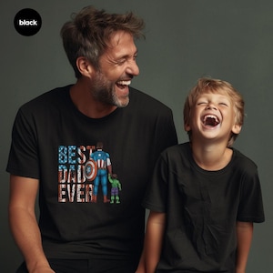 A man and a young boy are smiling and laughing together, both wearing black t-shirts with a graphic design.