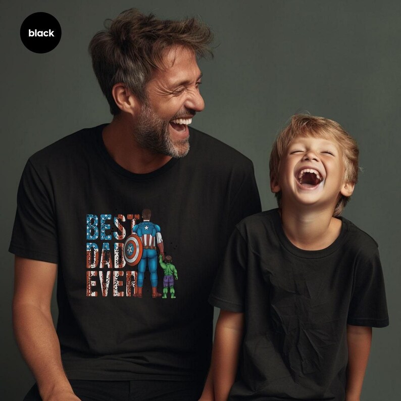A man and a young boy are smiling and laughing together, both wearing black t-shirts with a graphic design.