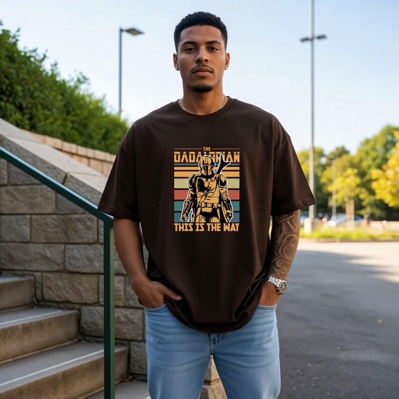 A man wearing a t-shirt with a graphic design of a character from the Star Wars franchise, standing in front of a stone wall and a staircase.