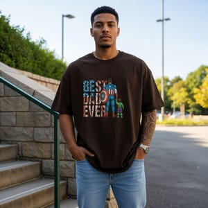 A man wearing a t-shirt with the text "BEST DAD EVER" standing in front of a stone wall and a staircase.