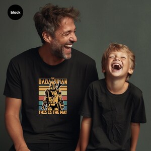 A man and a young boy are laughing and smiling together, both wearing black t-shirts with a graphic design featuring a character from the Star Wars franchise.