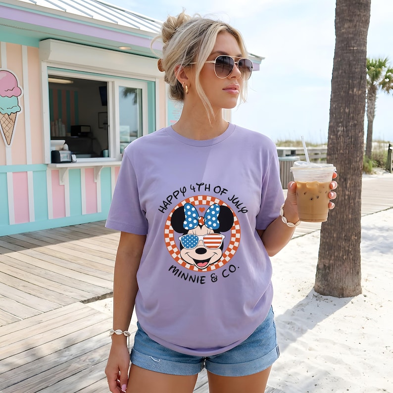 Blonde woman in sunglasses wearing a lavender Minnie Mouse "Happy 4th of July" tee, holding an iced coffee.
