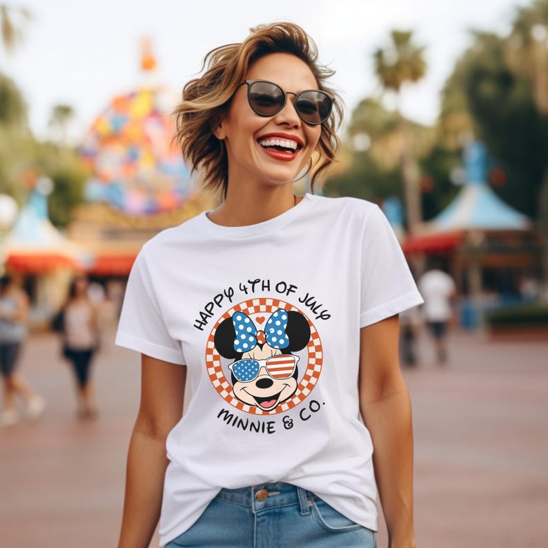 White t-shirt with Minnie Mouse in patriotic sunglasses, worn by smiling woman outdoors.