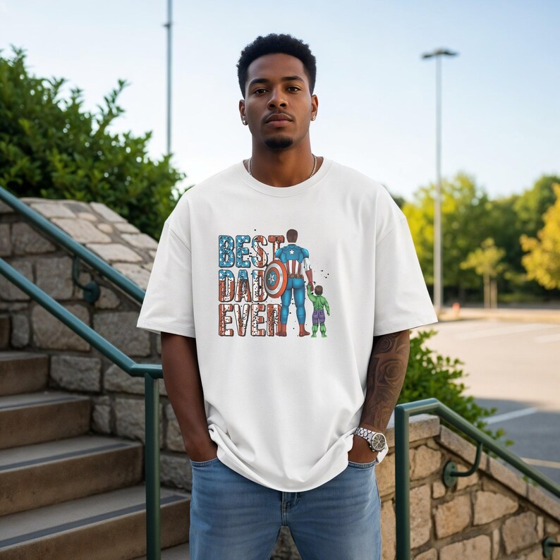 A man wearing a white t-shirt with a graphic design of a superhero and the text "Best Dad Ever" standing on a set of stairs.