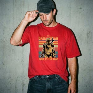 A man wearing a red t-shirt with a graphic of a character from the Star Wars franchise and the text "This is the way" printed on it.