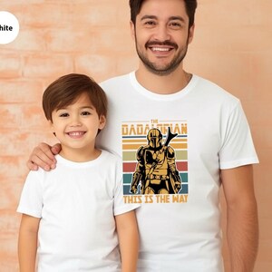 A young boy and an adult man wearing white t-shirts with a graphic of a character from the Star Wars franchise.