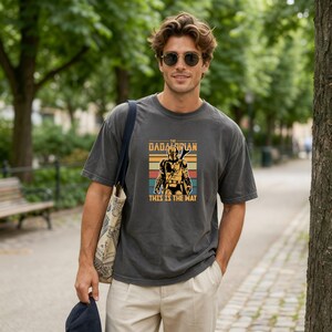 A man wearing a gray t-shirt with a graphic design and sunglasses is standing in a park.