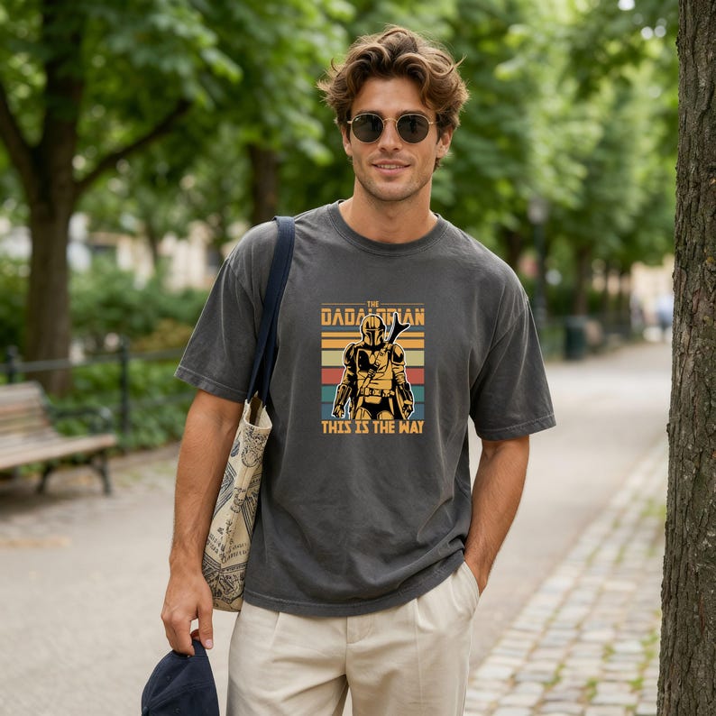 A man wearing a gray t-shirt with a graphic design and sunglasses is standing in a park.