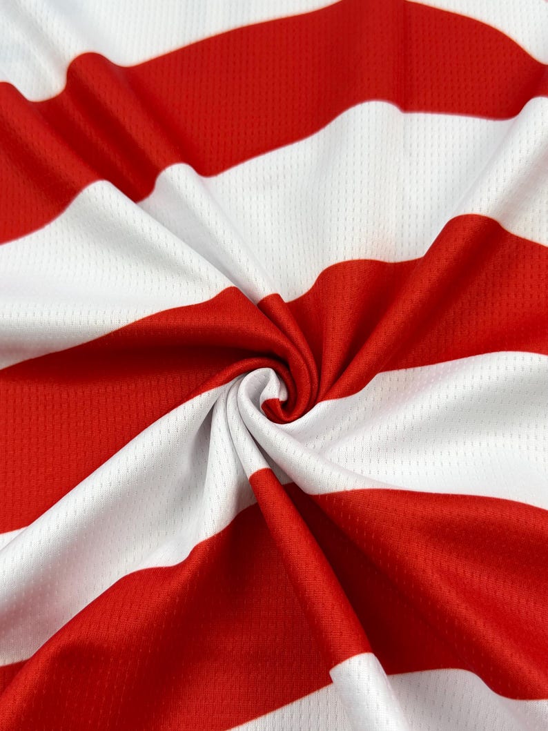 May include: A piece of athletic fabric featuring a repeating pattern of horizontal red and white stripes. The material has a visible mesh texture with small perforations throughout, and the fabric is gathered in the center to create folds.