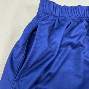 May include: A pair of royal blue athletic shorts featuring a textured, breathable mesh fabric. The shorts have an elasticized waistband with gathered fabric and a deep side pocket opening visible on the left side of the garment.
