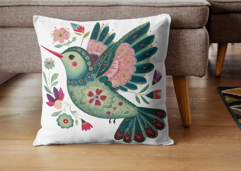 May include: White square throw pillow featuring a colorful illustration of a stylized bird with floral accents. The bird has teal, pink, and red details. The pillow is on a wooden floor next to a gray couch.