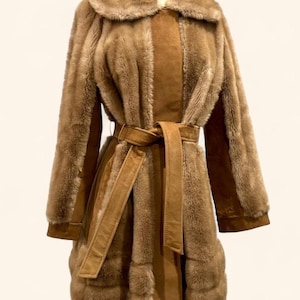May include: A vintage brown faux fur coat with a wide collar and a matching belt. The coat features a suede-like panel down the front and on the cuffs. The coat is displayed on a mannequin.