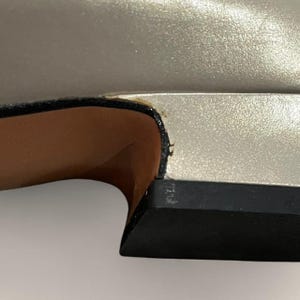 May include: Close-up of a silver shoe with a black sole. The shoe's upper has a metallic sheen, and the sole is a solid black. The interior of the shoe is a light brown color.