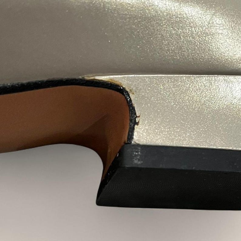 May include: Close-up of a silver shoe with a black sole. The shoe's upper has a metallic sheen, and the sole is a solid black. The interior of the shoe is a light brown color.