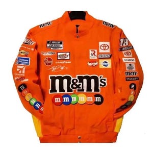 May include: An orange NASCAR racing jacket featuring the M&M's logo prominently on the chest. The garment is covered in various sponsor patches including Toyota, Snickers, and Goodyear, with colorful M&M candy graphics along the sleeves.