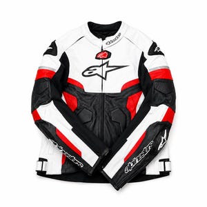 May include: A white, black, and red motorcycle jacket featuring the Alpinestars logo on the chest and sleeves. The jacket has a mandarin collar, a full-length front zipper, and protective paneling on the shoulders and arms with white accents.