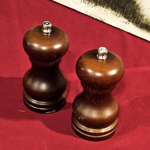 May include: A pair of wooden salt and pepper grinders. The grinders are dark brown with a bulbous shape and silver-colored tops. The salt grinder is marked with a "P" and the pepper grinder is marked with an "S".