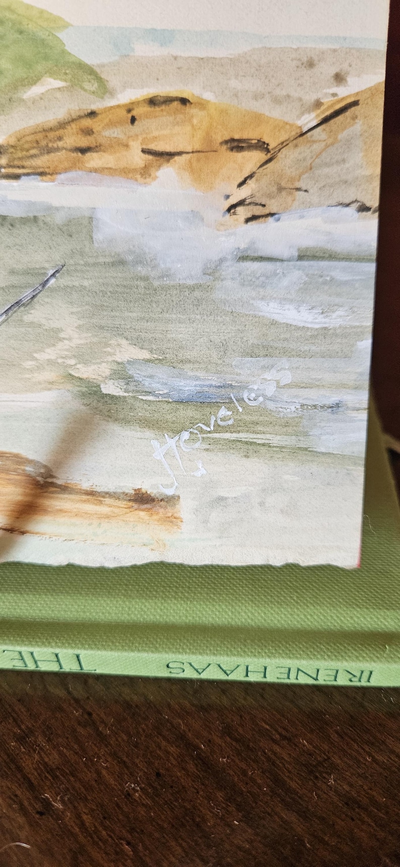 Pu&ograve; includere: Dipinto ad acquerello di un paesaggio costiero con toni tenui di verde, beige e blu. L'opera presenta una linea di costa con uno sperone roccioso e la firma dell'artista, "Hovels". Il dipinto &egrave; su carta.