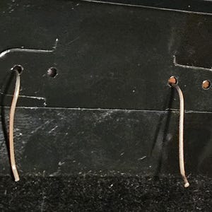 Puede incluir: Un par de pendientes delicados y finos, de color plateado, colgando de una tarjeta de exhibici&oacute;n de pendientes negra. Los pendientes son sencillos, con un dise&ntilde;o curvo similar a un alambre. La tarjeta tiene dos agujeros para colgar los pendientes.