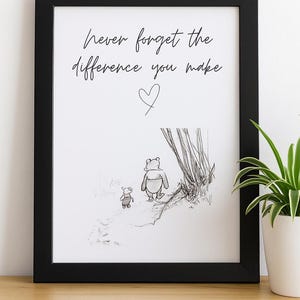 Könnte beinhalten: Schwarz gerahmter Druck mit dem handschriftlichen Zitat "Vergiss nie den Unterschied, den du machst". Darunter eine Skizze von Winnie Puuh und Ferkel, mit einem Herzsymbol. Im Hintergrund ist eine Topfpflanze zu sehen.