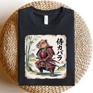 May include: Black t-shirt featuring a capybara in samurai armor with a sword. The graphic includes Japanese text and bamboo stalks. The shirt is made of a soft material and is suitable for casual wear.