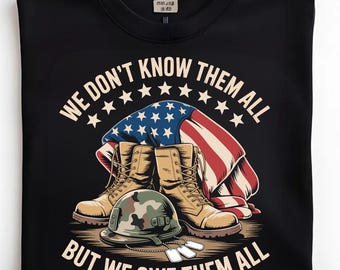 Puede incluir: Camiseta negra con un gráfico de botas militares, un casco, chapas de identificación y una bandera estadounidense. El texto dice: "WE DON'T KNOW THEM ALL BUT WE OWE THEM ALL."