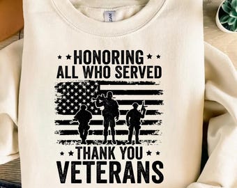 Puede incluir: Sudadera de color crema con un diseño gráfico en honor a los veteranos. El diseño presenta el texto "HONORING ALL WHO SERVED" y "THANK YOU VETERANS" encima y debajo de una bandera estadounidense estilizada con siluetas de soldados.