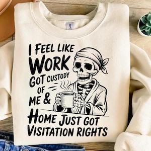 May include: Cream-coloured sweatshirt with the text "I FEEL LIKE WORK GOT CUSTODY OF ME & HOME JUST GOT VISITATION RIGHTS." A black and white illustration of a skeleton wearing a robe and holding a mug is featured on the front.
