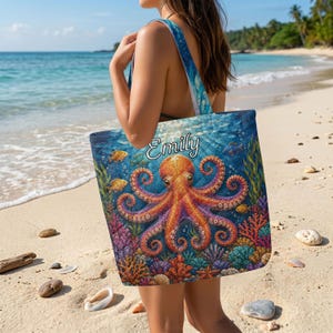 May include: A blue tote bag with an orange octopus design, coral, fish, and the name "Emily". The bag has blue straps and is held on a beach with the sea in the background.