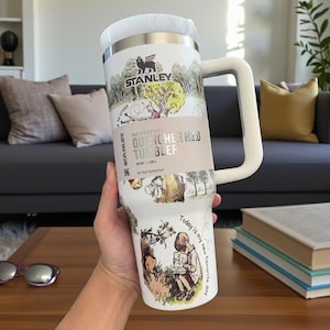 May include: White Stanley Quencher H2.0 tumbler with a large handle. The tumbler features illustrations and text, including "Stanley" and "Today is my new favorite day." It holds 40 oz (1.18 L).