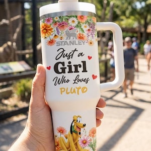 Puede incluir: Vaso Stanley blanco con diseño floral y el texto "Just a Girl Who Loves Pluto". El vaso presenta un gráfico de Pluto y un asa blanca. Incluye tapa y pajita blancas.