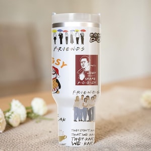Puede incluir: Un vaso de acero inoxidable blanco con varios gr&aacute;ficos y texto de la serie de televisi&oacute;n "Friends". El dise&ntilde;o incluye personajes de dibujos animados, el logotipo del programa y citas. El vaso tiene una tapa blanca y un borde plateado.