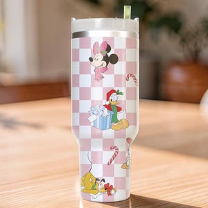 May include: A stainless steel tumbler with a white lid and a pink and white checkered pattern. The tumbler features cartoon characters Minnie Mouse, Donald Duck, Pluto, and candy canes. The characters are dressed in holiday attire.