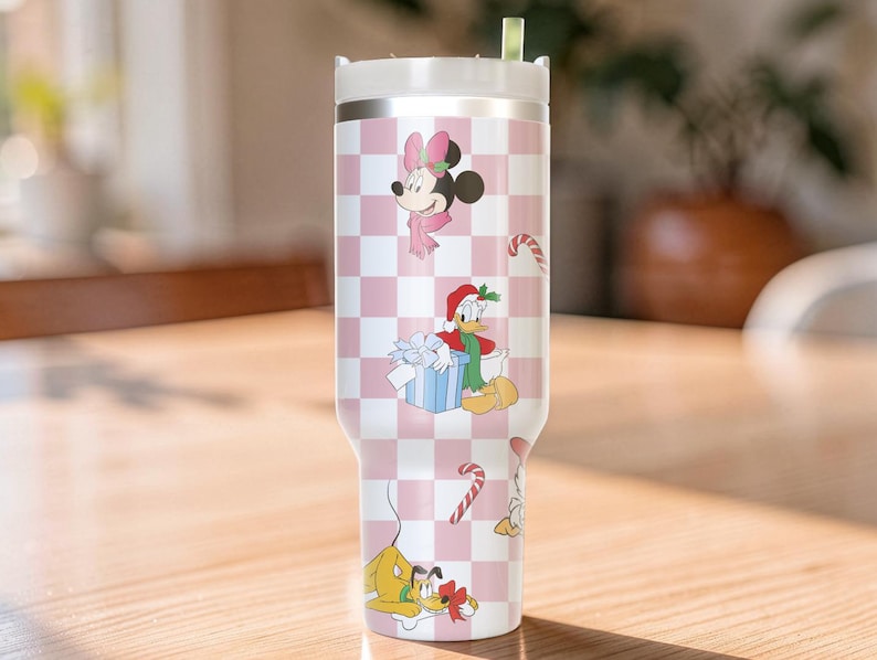 May include: A stainless steel tumbler with a white lid and a pink and white checkered pattern. The tumbler features cartoon characters Minnie Mouse, Donald Duck, Pluto, and candy canes. The characters are dressed in holiday attire.