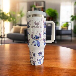 K&ouml;nnte beinhalten: Ein wei&szlig;er Stanley-Becher mit einem Stitch-Cartoon-Design. Der Becher hat einen Griff und einen wei&szlig;en Deckel. Die Stitch-Figur ist in verschiedenen Posen dargestellt, mit floralen und sternf&ouml;rmigen Akzenten. Das Stanley-Logo ist sichtbar.
