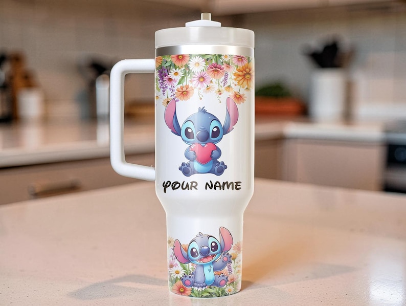Puede incluir: Un vaso t&eacute;rmico blanco con asa, con un dise&ntilde;o floral y un personaje de dibujos animados sosteniendo un coraz&oacute;n. El texto "YOUR NAME" est&aacute; impreso en el vaso. El vaso tiene una capacidad aproximada de 887 ml.