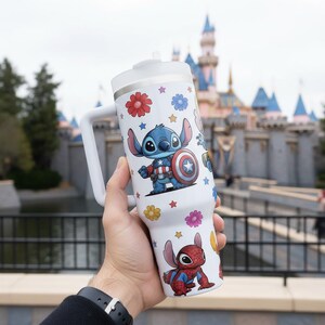 May include: White tumbler with a handle, featuring colorful cartoon illustrations of Stitch as Captain America and Spider-Man. The tumbler has a white lid and a straw. Floral and star designs are also present.